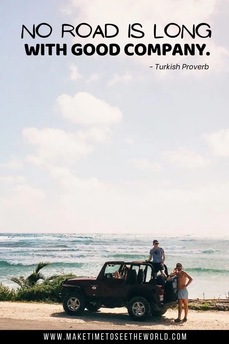 An open top jeep parked at the side of the road in front of the ocean with one guy standing in the car and one next to it with text overlay No road is long with good company