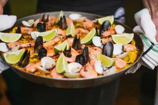 Paella pan filled with a paella topped with muscles, mushrooms, lime wedges and prawns