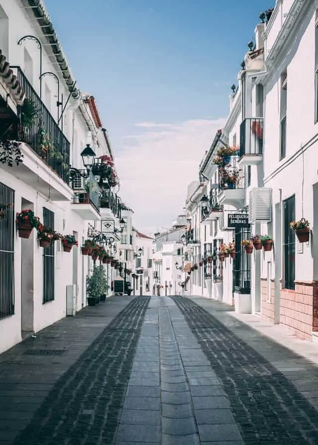 Narrow street in a spanish town with while two storey buildings lining each side of the paved central street