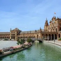 Cover photo for the Top Spain Travel Tips featuring the plaza in Seville with a palatial building standing beside a curved body of water
