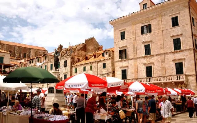 Red and white beach umberellas cover open air market stalls with stonewashing buildings in the background