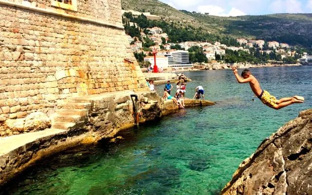 People swimming in the clear blue water outside the high walls of Dubrovniks Old Town