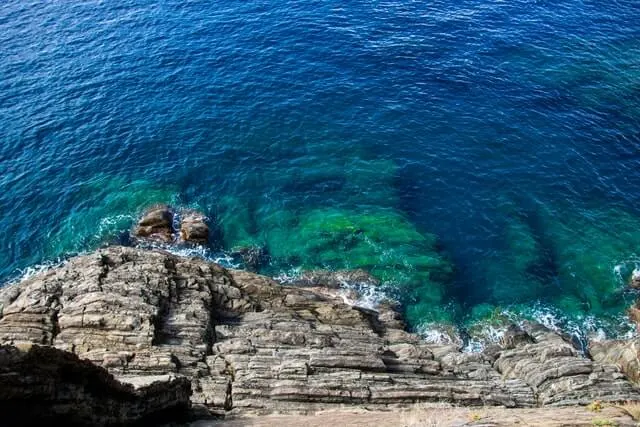 View looking down on a rugged rocky coastline where it meets the clear blue ocean
