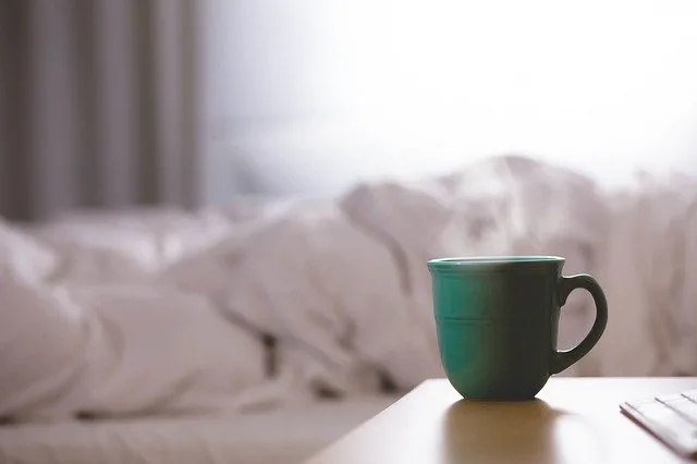 Green Coffee Mug on a wooden table next to a slept in bed