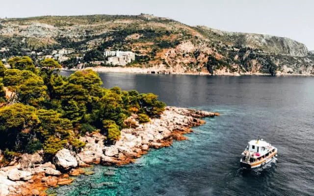 Rocky shoreline of Lokrum Island next to light blue ocean with the Croatian mainland in the background