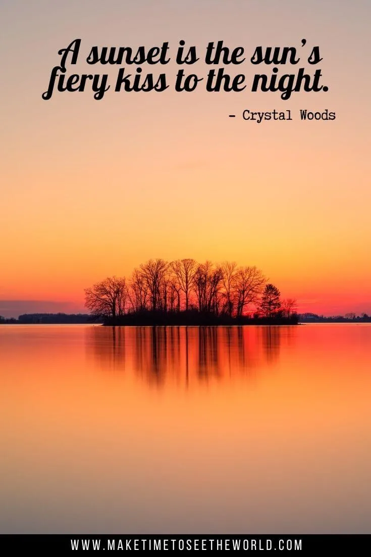 A sunset is the sun’s fiery kiss to the night." - Crystal Woods text overlay above a lake with a small island in the middle under an orange sunset sky