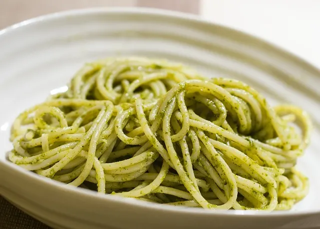 White bowl containing spaghetti covered in pesto