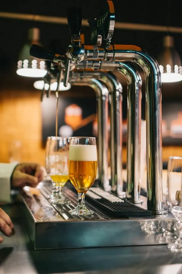 4 Shiny silver beer taps with two half pint glasses underneath the spouts, one glass full of beer, one being filled