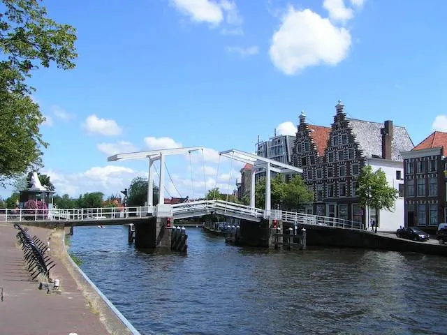 River with a white wooden bridge across and buildings on the far river bank