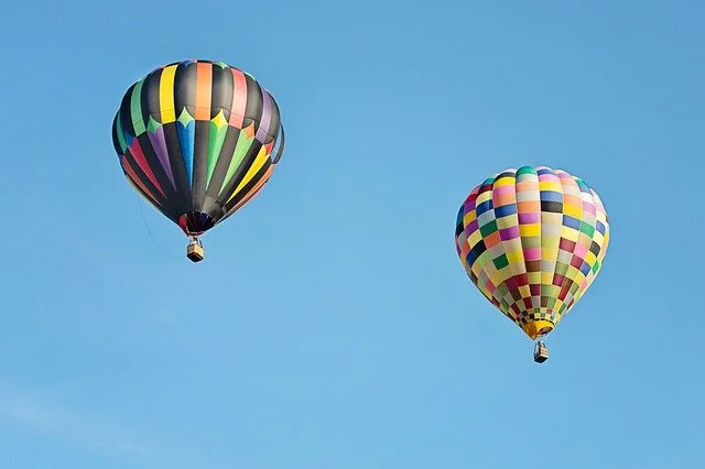 Two multicoloured hot air balooons flying high in the blue sky