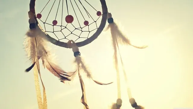 Dreamcatcher with feathers hanging from the loop in front of a sunburst