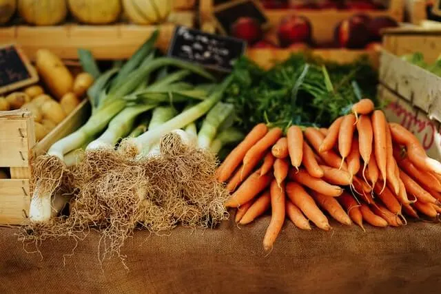 Fresh vegetables (wooden box of patoatoes next to loose leeks and carrots) lying on a wooden table at a farmers market