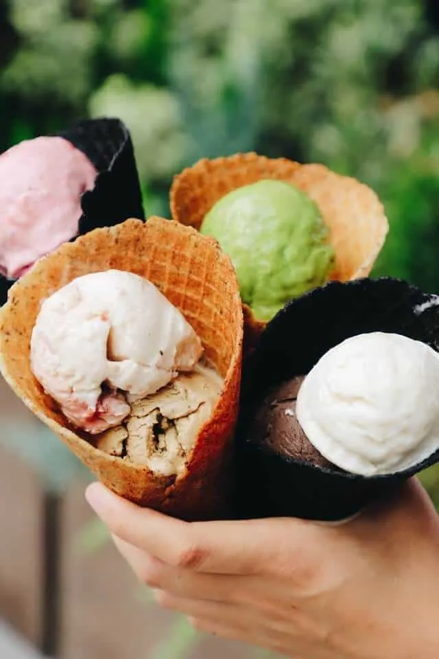 Hand holding 4 different coloured ice-cream cones with different flavour ice-cream balls within the waffle cones