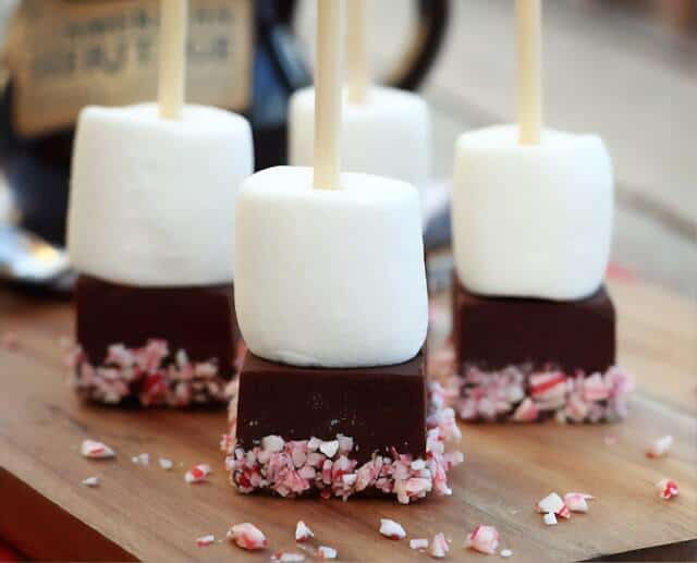 White marshmellow on a square chocolate block topped with pink sprinkes on sticks places upside down on a wooden board