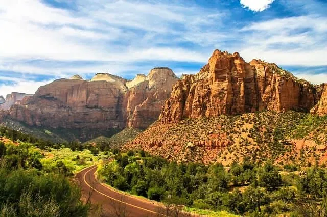 Zion Canyon Scenic Drive Aerial shot of the road snaking around the base of the rocky peaks under a blue sky with whisoy white clouds