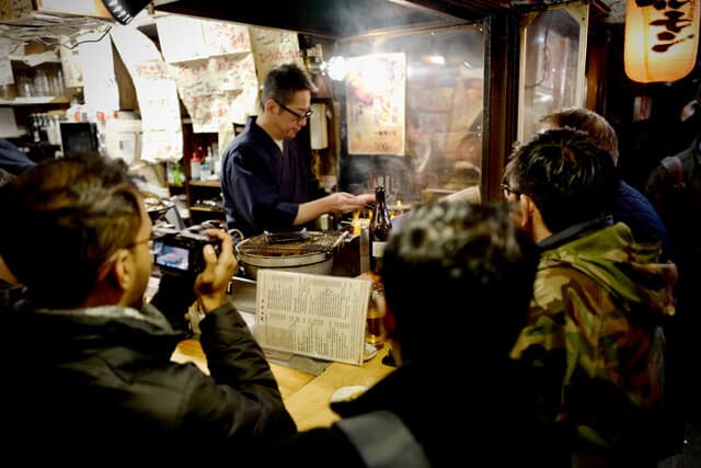 Customers sitting around a small Bar and Restaurant known as an Izakaya 