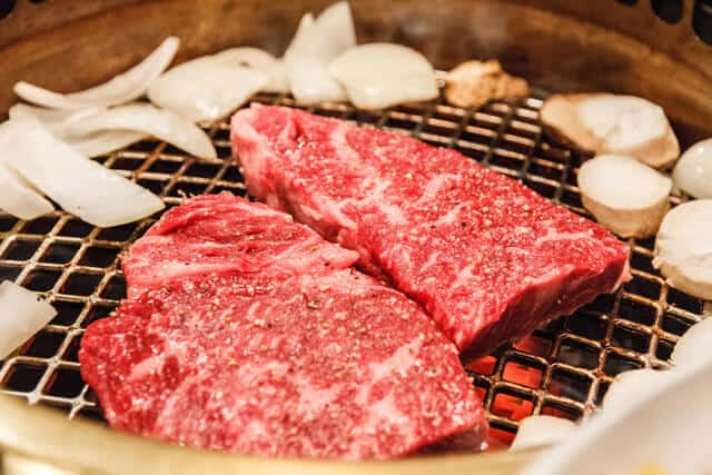 Bright red kobe beef steaks on a cast iron grill with fire underneath