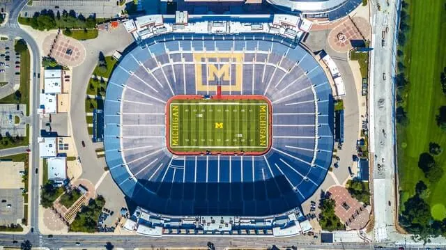 Top down shot of the Big House Stadium with green rectangylar playing field at the centre surrounded by thousands and thousands of blue seats