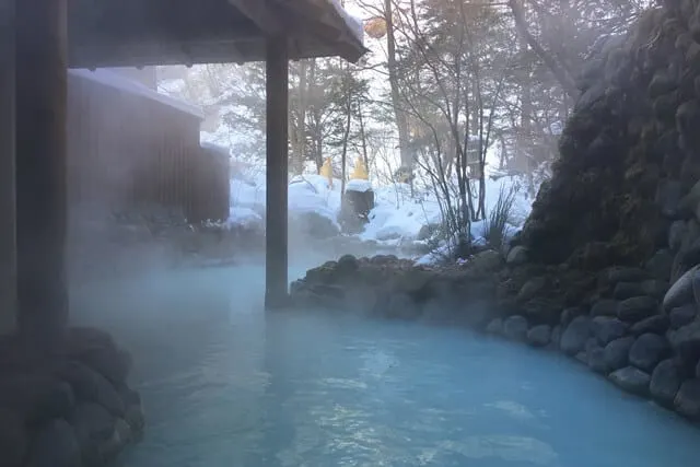 Outdoor Onsen with steaming hot blue water surrounded by snow covered trees