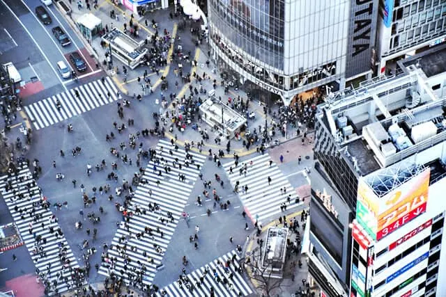 Aerial view of the manic Shibuya Crossing with three diferent zebra crossings going in different directions each covered with people and surrounded by skyscrapers