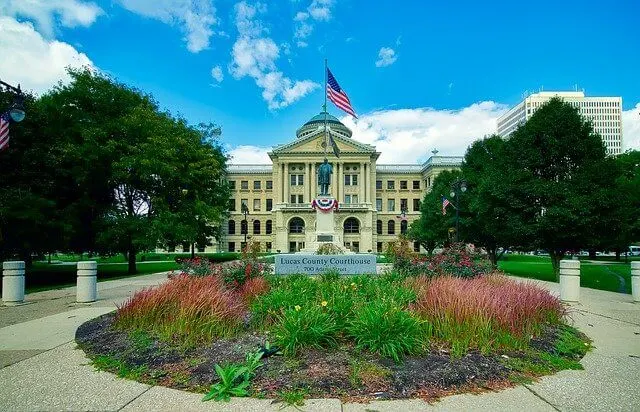 Large white town hall building with the American flag flying above and a sculpted garden in front