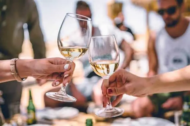 Two white wine glasses clinking together in focus in front of a crowd of people
