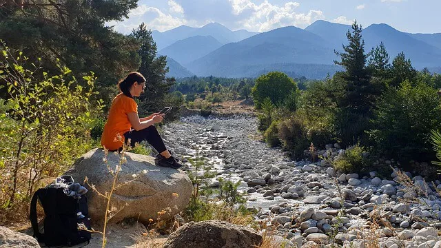 Woman on an ipad sitting on a boulder next to a river in Nature