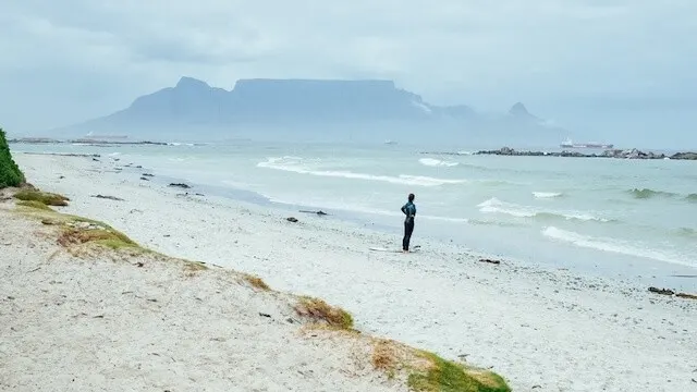 Woman standing in the distance on the ebach at the oceans edge with Table Mountain in the distance behind the woman