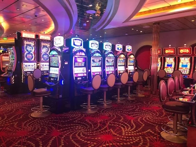Mariner of the Seas Casino deck with multiple gambling machines bathed in yellow and purple lights on a red patterned carpet