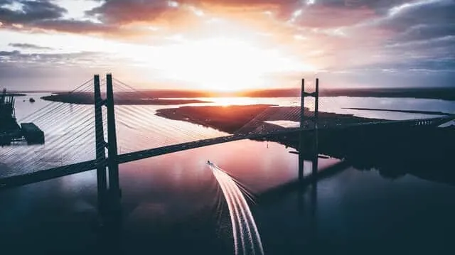 Jacksonville bridge at sunrise, bridge in silohuette with a speedboad sailing underneath leaving a wake trail behind