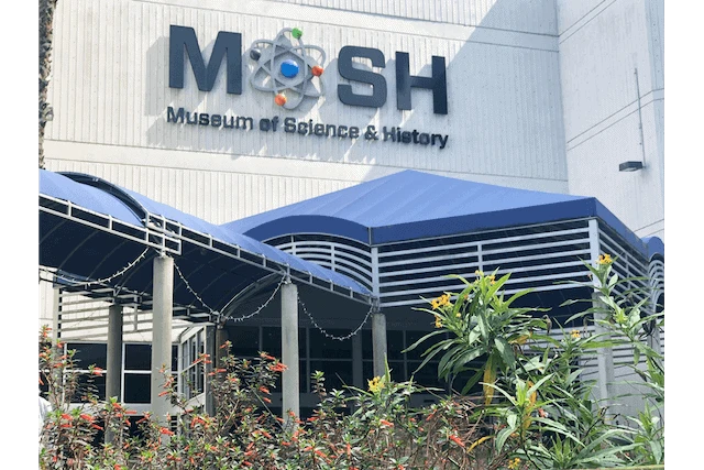 Large MOSH sign on the side of a white building with a blue covered walkway leading to the door under the sign