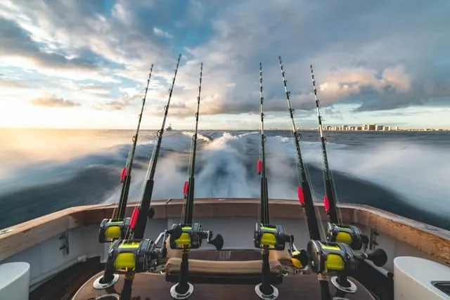 4 Fishing lines at the back of a small boat with the wake behind and a city skyline in the distance