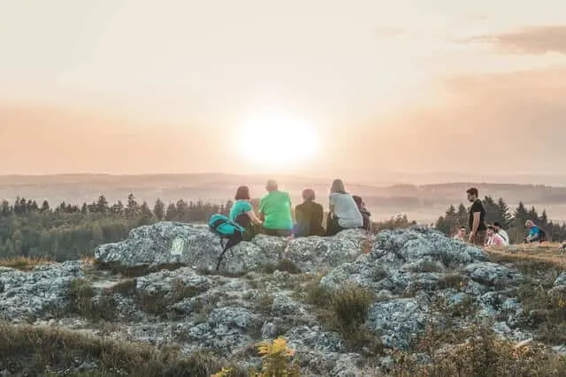 Group of hikers watching the sunset taking a break sitting on top of a rock