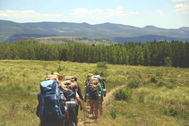 Group of hikers carrying backpacks down a dirt path heading towards a forrest in the distance