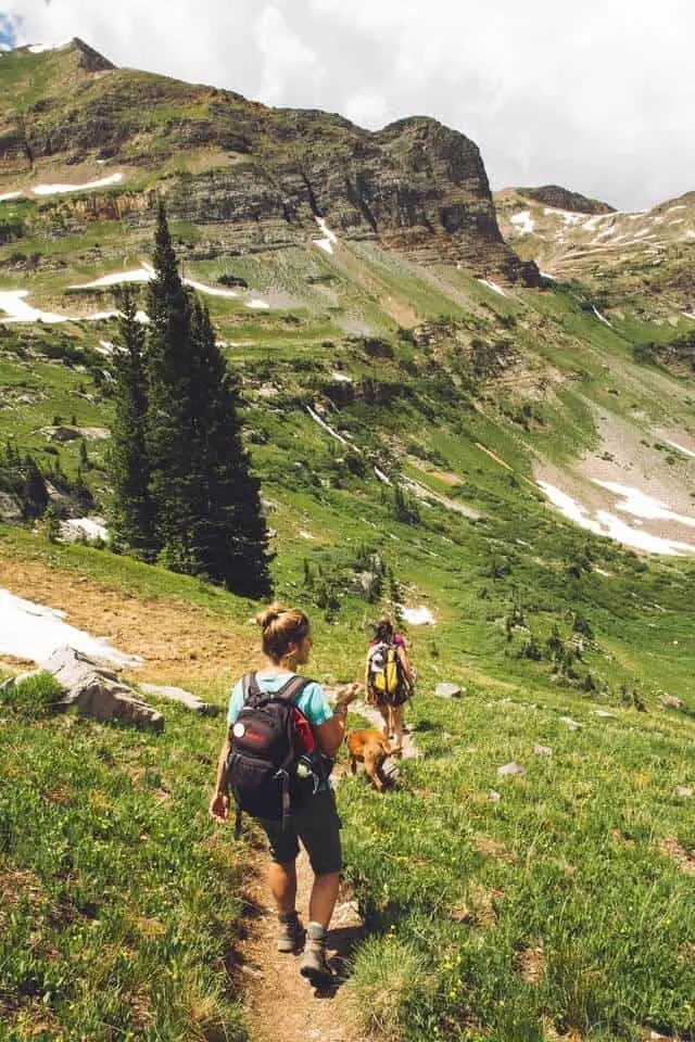 Two female hikers walking down a mountainside grass covered trail