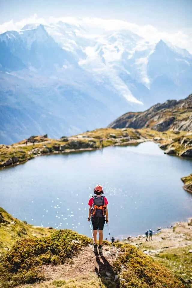 Woman standing on a rock in front of a mountain lake with a sheer drop at the edge of the water