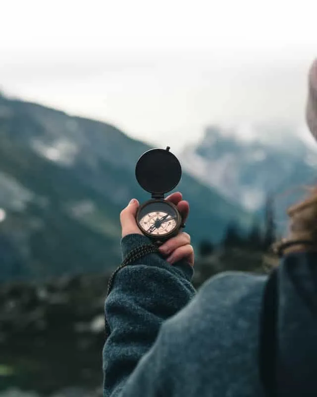 Woman holding an old fashioned compass in front of a misty mountain background