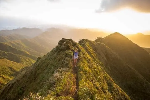 Woman hiking with no hiking essentials on a mountain top path at sunset