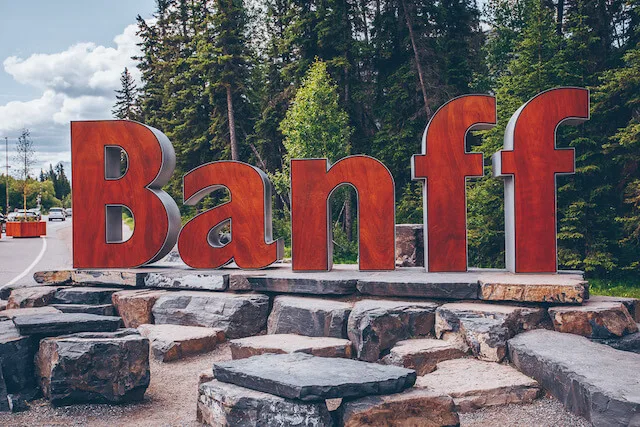 Banff Town Sign - large letters in red on top of a rocky platform with tall fir trees behind it