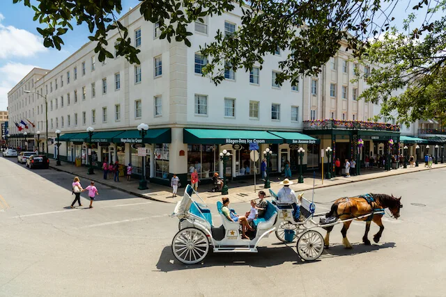 Corner of downtown San Antonio, a white multistorey building on the corner with a horse drawn carriage on the road in the foreground