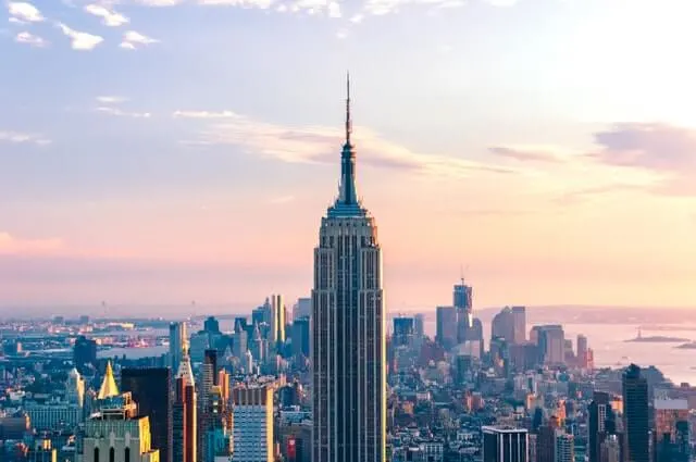 Iconic spire of the Empire State Building NYC standing taller than all the other buildings around it under a light pink sky at dusk