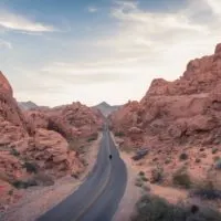 Epic Road Trips from Las Vegas cover photo of a person standing in the middle of the road between a valley of red rocky outcrops