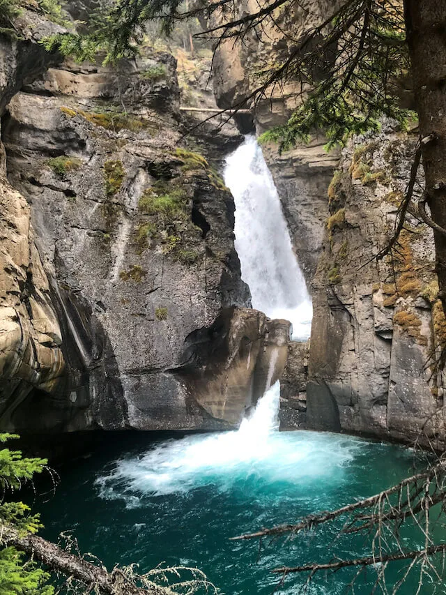 Small waterfall crashing down a rocky cliff into a dark pool of water at Johnstons Canyon