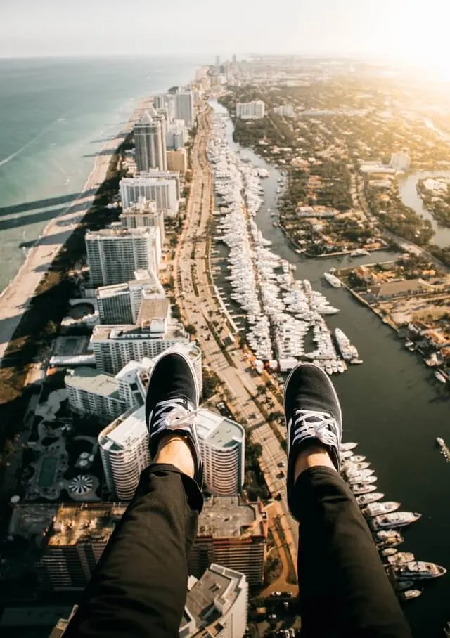 Womans feet wearing back trainers sticking out over the city of Miami below, while flying in a helicopter