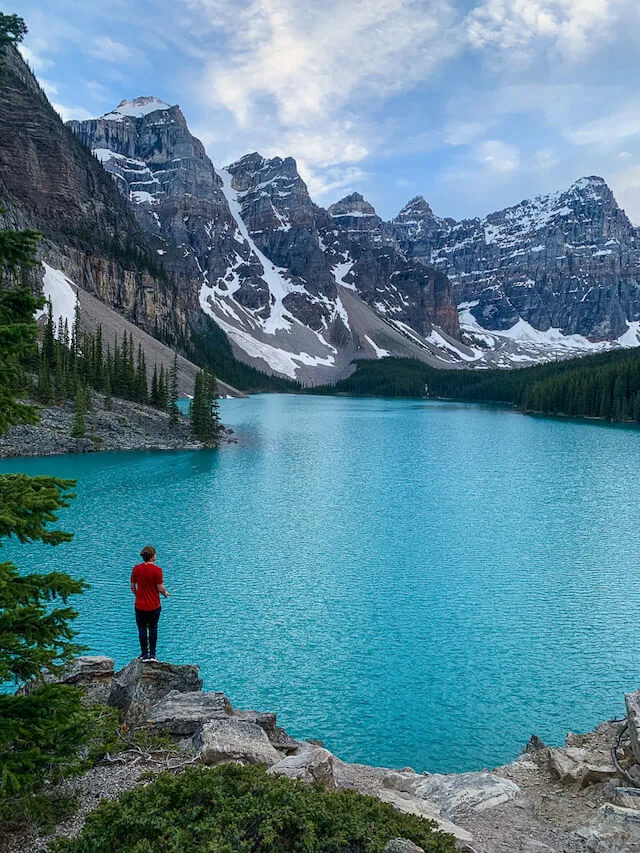 Vibrant blue Moraine Lake, surrounded by the rocky mountains with a person wearing a red jacket standing in the foreground