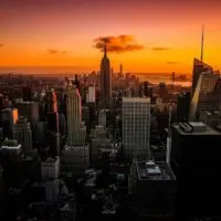 Perfect Itinerary for One Day in New York City (By A Local) header image of the New York skyline from above at sunset backed by shaed of orange and purple