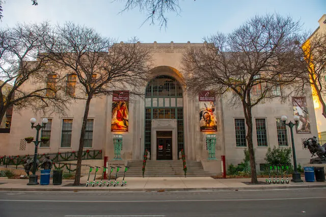 Facade of the San Antonio Museum of Art flanked by trees with no leaves on their brances on either side of the doorway