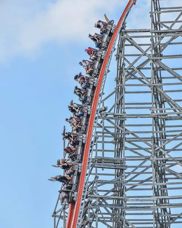 Vertical wooden rollar coaster, the carriage rolling down the track, people have their arms and hands in the air