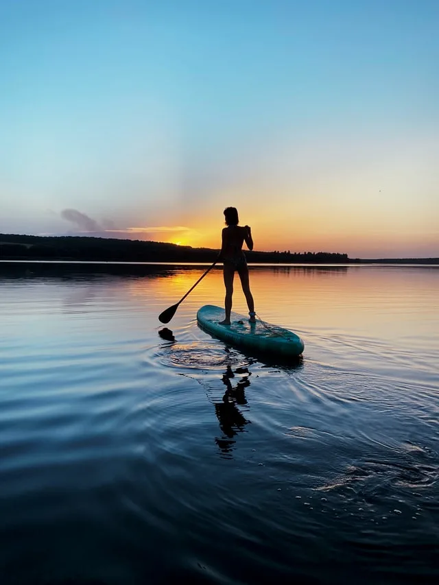 Woman on a Stand Up Paddle Board on flat water at sunrise with a rocky ridge in the background