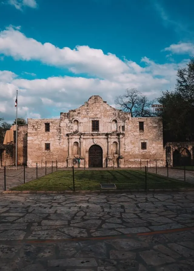 The Front Facade of the ALamo, a white double story building under a blue sky with white clouds